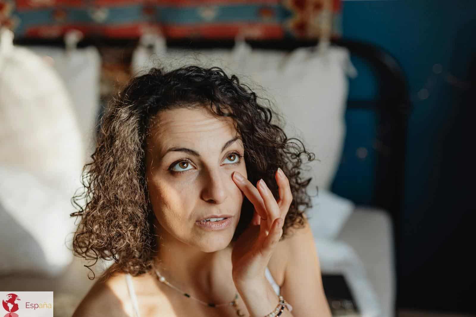 Woman applying skincare in a sunlit bedroom, embracing morning relaxation and self-care.