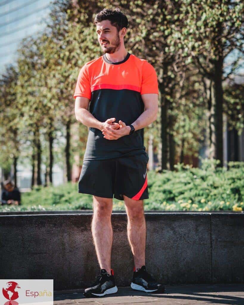 man in red nike crew neck t-shirt and black shorts standing on gray concrete pavement